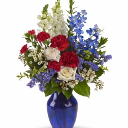 Mixed bouquet of red carnations, white roses, and blue flowers in a cobalt vase