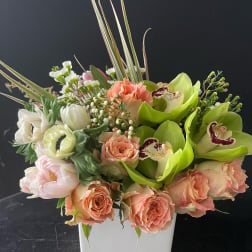 Mixed bouquet in a white square vase with peach roses and green orchids