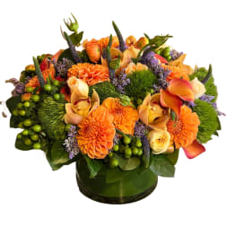 Orange and peach floral arrangement in a green glass vase