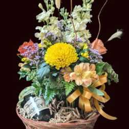 Basket arrangement with yellow and peach flowers and a wine bottle