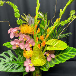 Tropical arrangement with pink orchids, yellow pincushion blooms, and anthuriums in a glass vase