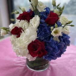 Red roses and white blooms arranged with blue hydrangeas in a glass vase