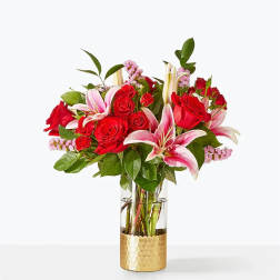 Red roses and pink lilies arranged in a glass vase with a gold base