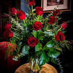 Red roses arranged in a clear glass vase with mixed greenery