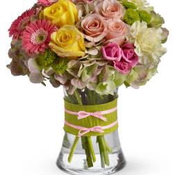 Mixed bouquet of pink gerberas, roses, hydrangeas and yellow roses in a clear vase with green ribbon