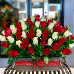 Red and white roses arranged in a rectangular box with a red ribbon