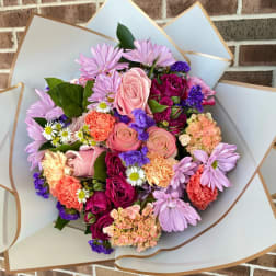 Mixed bouquet of pink, purple, and peach flowers wrapped in white paper