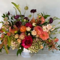 Large mixed bouquet in a white vase with pink, peach, and burgundy blooms