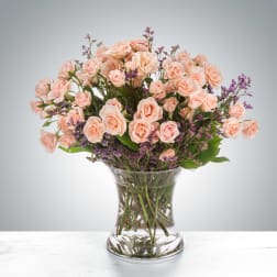 Peach roses and purple filler flowers in a clear glass vase