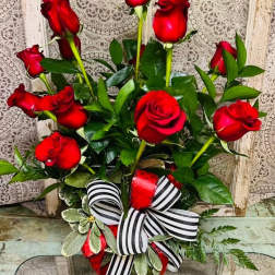 Red roses arranged in a glass vase with a striped ribbon bow