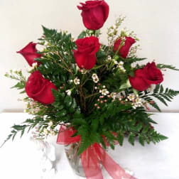 Red roses arranged in a clear glass vase with greenery and a red ribbon