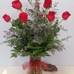 Red roses arranged in a glass vase with a red ribbon