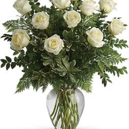 White roses arranged in a clear glass vase with mixed greenery