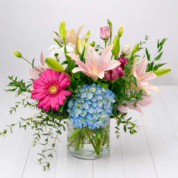 Mixed bouquet with pink lilies, blue hydrangea, and a pink gerbera daisy in a glass vase