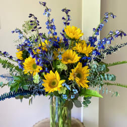 Bouquet of yellow sunflowers and blue flowers in a glass vase
