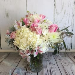 Pink roses and white mixed flowers arranged in a clear glass vase