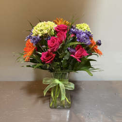 Mixed bouquet of pink roses, purple daisies, and orange blooms in a glass vase