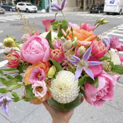 Handheld bouquet of pink, peach, and purple flowers in a glass vase