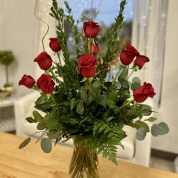 Red roses arranged in a clear glass vase with mixed greenery