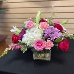Mixed pink, white, and purple flower arrangement in a square glass vase