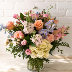Mixed bouquet of pink, peach, lavender, and white flowers in a glass vase