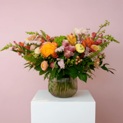 Mixed bouquet of orange, pink, and white flowers in a ribbed glass vase