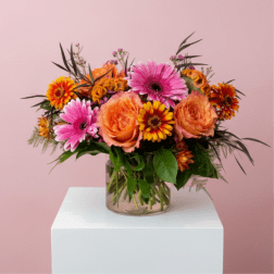 Mixed bouquet of orange and pink flowers in a clear glass vase