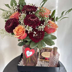 Bouquet of burgundy chrysanthemums and peach roses in a vase with chocolates and perfume