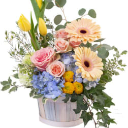 Mixed bouquet in a wooden basket with yellow tulips, pink roses, and gerbera daisies