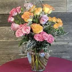 Arrangement of pink, orange, and yellow roses with white filler flowers in a clear glass vase.