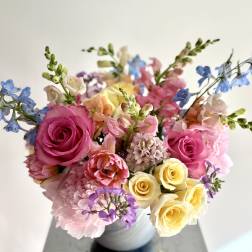 Mixed bouquet of pink, yellow, and blue flowers in a white vase