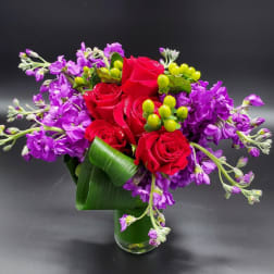 Red roses and purple flowers arranged in a glass vase