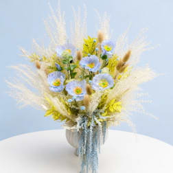 Tall pastel bouquet with blue flowers and dried grasses in a white vase