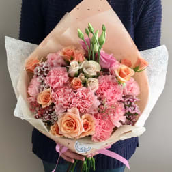 Handheld bouquet of pink and peach roses with carnations wrapped in paper