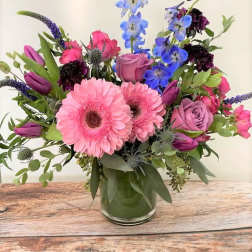 Mixed pink, purple, and blue flowers arranged in a clear glass vase