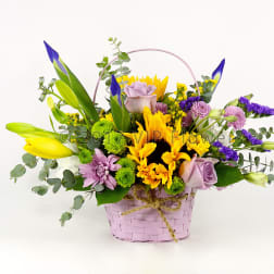 Mixed bouquet in a pink basket with yellow, purple, and lavender flowers