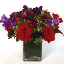 Red roses and purple flowers in a square glass vase