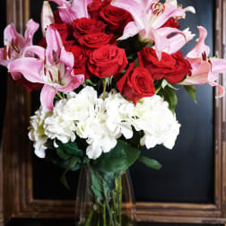 Bouquet of red roses, pink lilies, and white hydrangeas in a glass vase