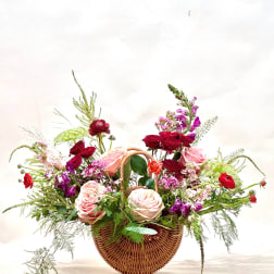 Basket arrangement of pink and red roses with purple flowers