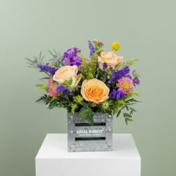 Mixed bouquet of peach roses and purple flowers in a metal crate