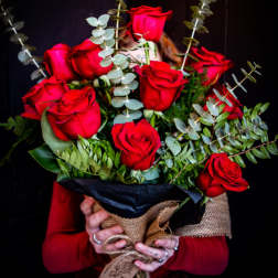 Hand-tied bouquet of red roses wrapped in burlap and black paper, held against a dark background