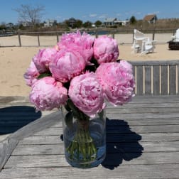Pink peonies arranged in a clear glass vase on a wooden table.