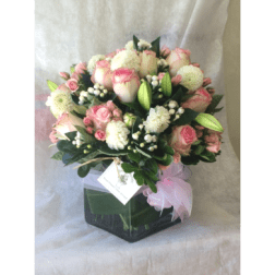 Pink and white bouquet in a square glass vase with a pink ribbon
