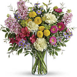Mixed bouquet of pink, yellow, purple, and white flowers in a glass vase