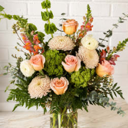 Mixed bouquet of peach roses, cream blooms, and green flowers in a glass vase