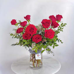 Red roses arranged in a clear glass vase with greenery