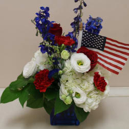 Red, white, and blue floral arrangement with an American flag in a blue vase