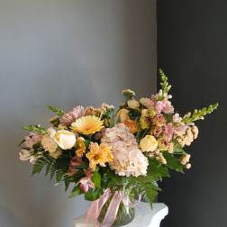 Pastel mixed flower arrangement in a glass vase with pink ribbon