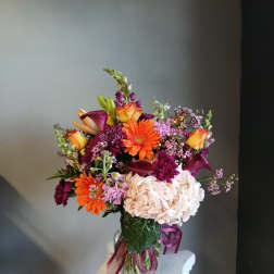 Mixed bouquet of orange, purple, and white flowers in a glass vase