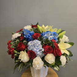 Mixed bouquet of red roses, blue hydrangeas, white carnations, and pale lilies in a white vase